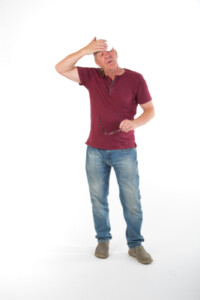 A person standing and mopping sweat from his brow after using a hand pump for a long time.