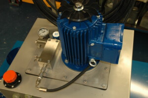 a blue electric motor for a hydraulic pump and control manifold mounted on top of a reservoir. Pressure gauge and regulator know are visible.