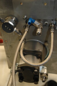 Underside of hydraulic reservoir with parts mounted on lid and connections underneath including hoses